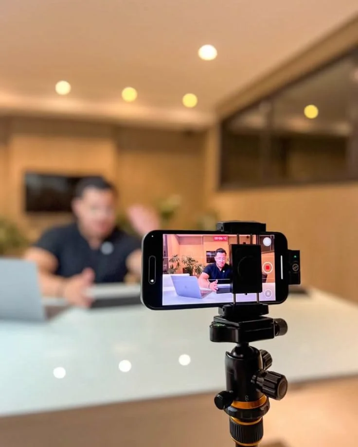 A phone on a tripod filming a man working at his desk